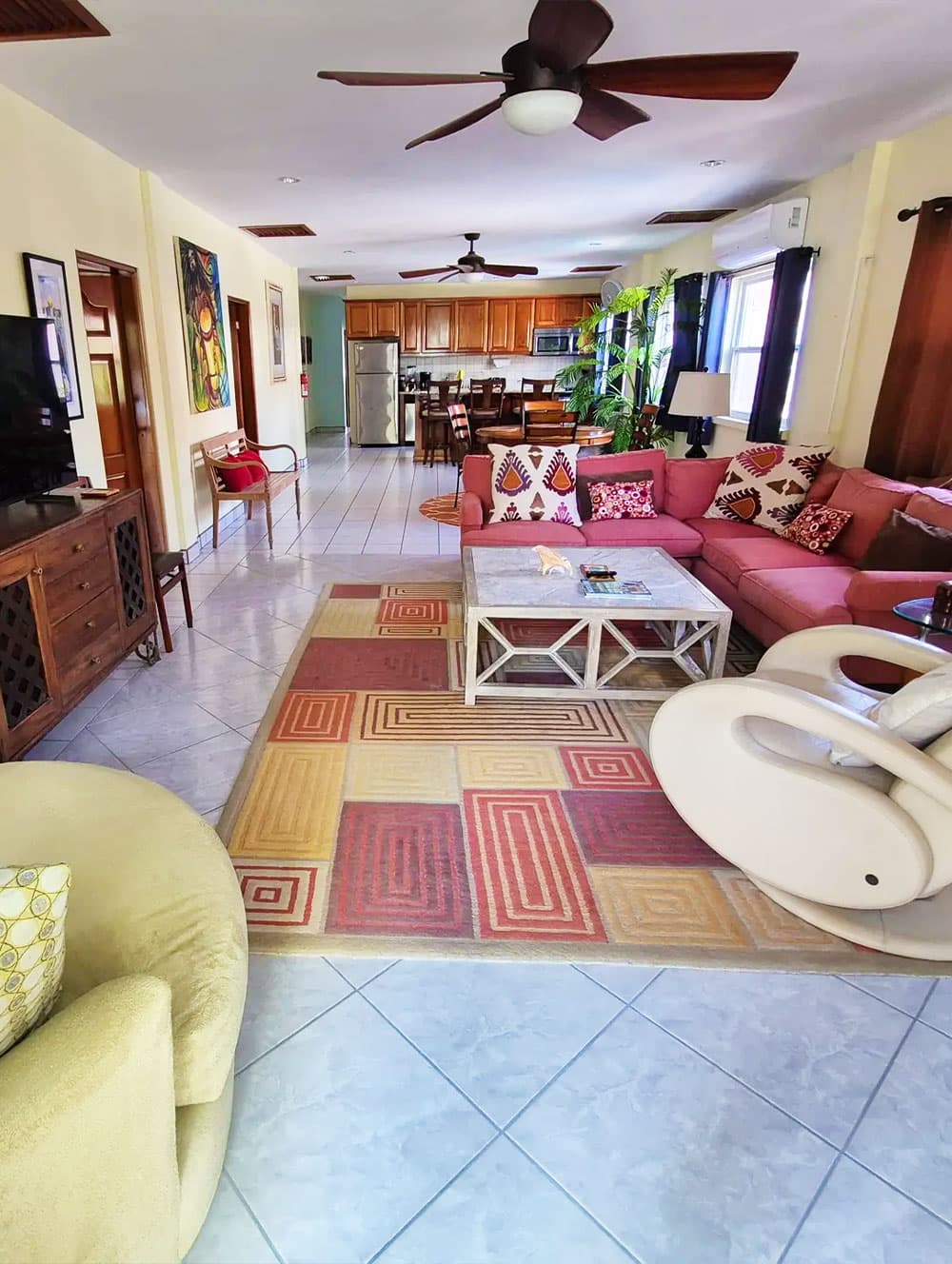 A spacious living room featuring a pink sectional couch, a coffee table, and an open kitchen with wooden cabinetry.