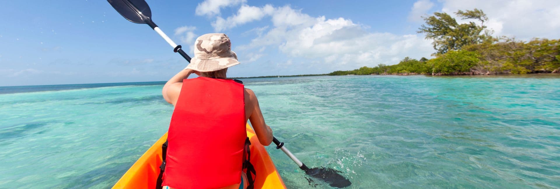 A person in a red life vest paddles a kayak through clear turquoise water.