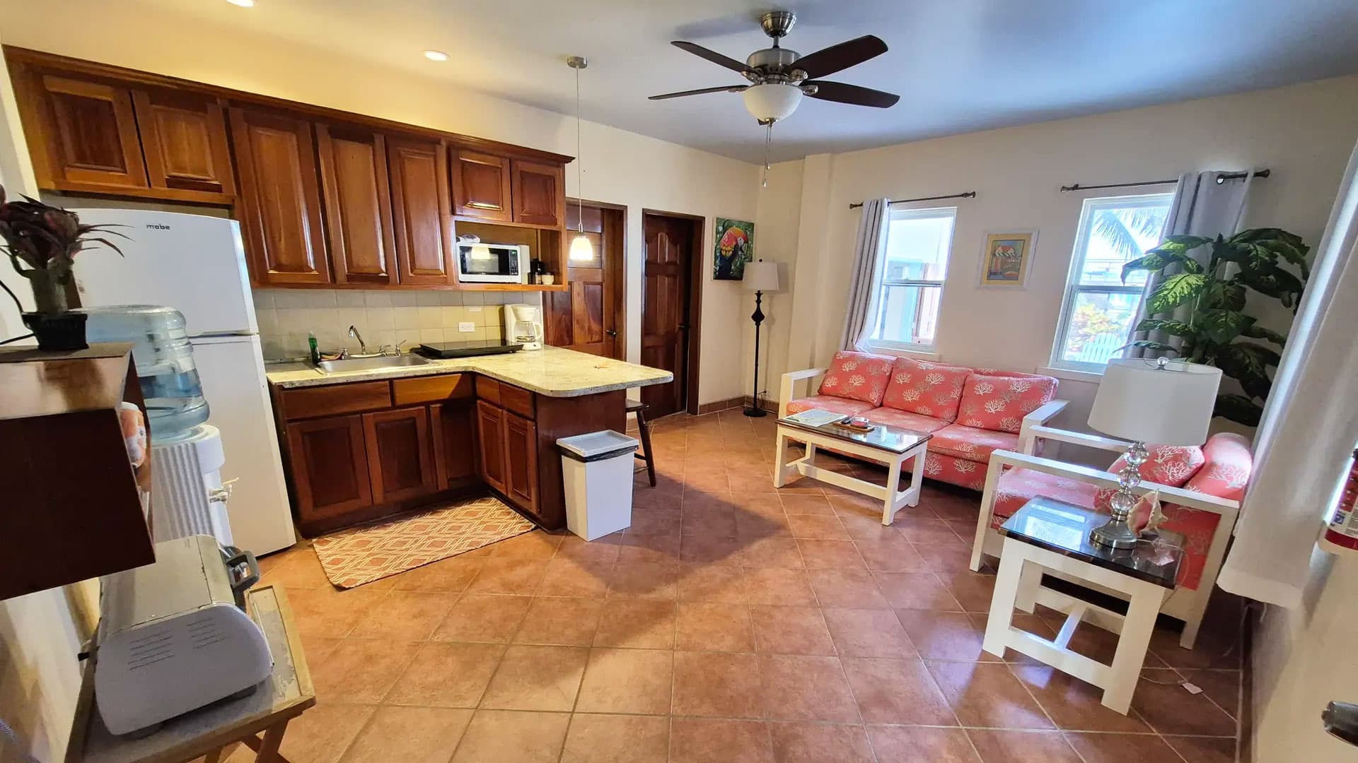 A cozy kitchen and living area featuring wooden cabinets, a sofa, and natural light from windows.